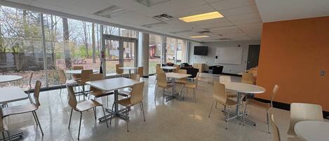 A spacious cafeteria with high ceilings, large windows, and a mix of tables and chairs.