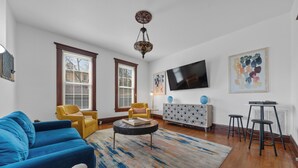 Un salon avec un canapé bleu, un fauteuil jaune, une table basse ronde et un téléviseur fixé au mur.