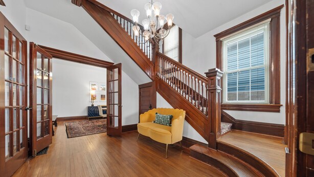 Une pièce spacieuse avec un escalier en bois, un canapé jaune et un lustre.