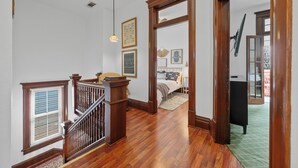 Un escalier avec des rampes et une main courante en bois, menant à une chambre à coucher équipée d’un lit et d’une table de chevet.