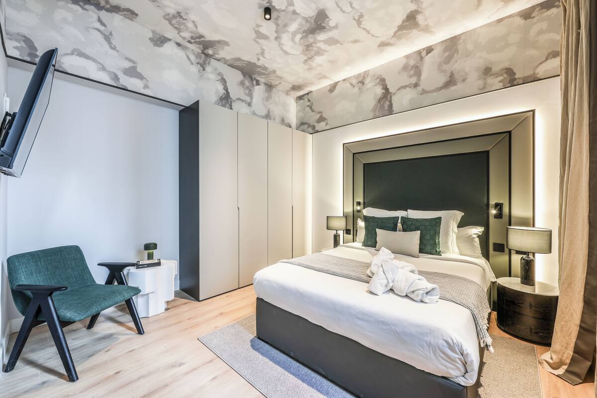 Een moderne slaapkamer met een bed, nachtkastjes, een stoel en een aan de muur bevestigde televisie.