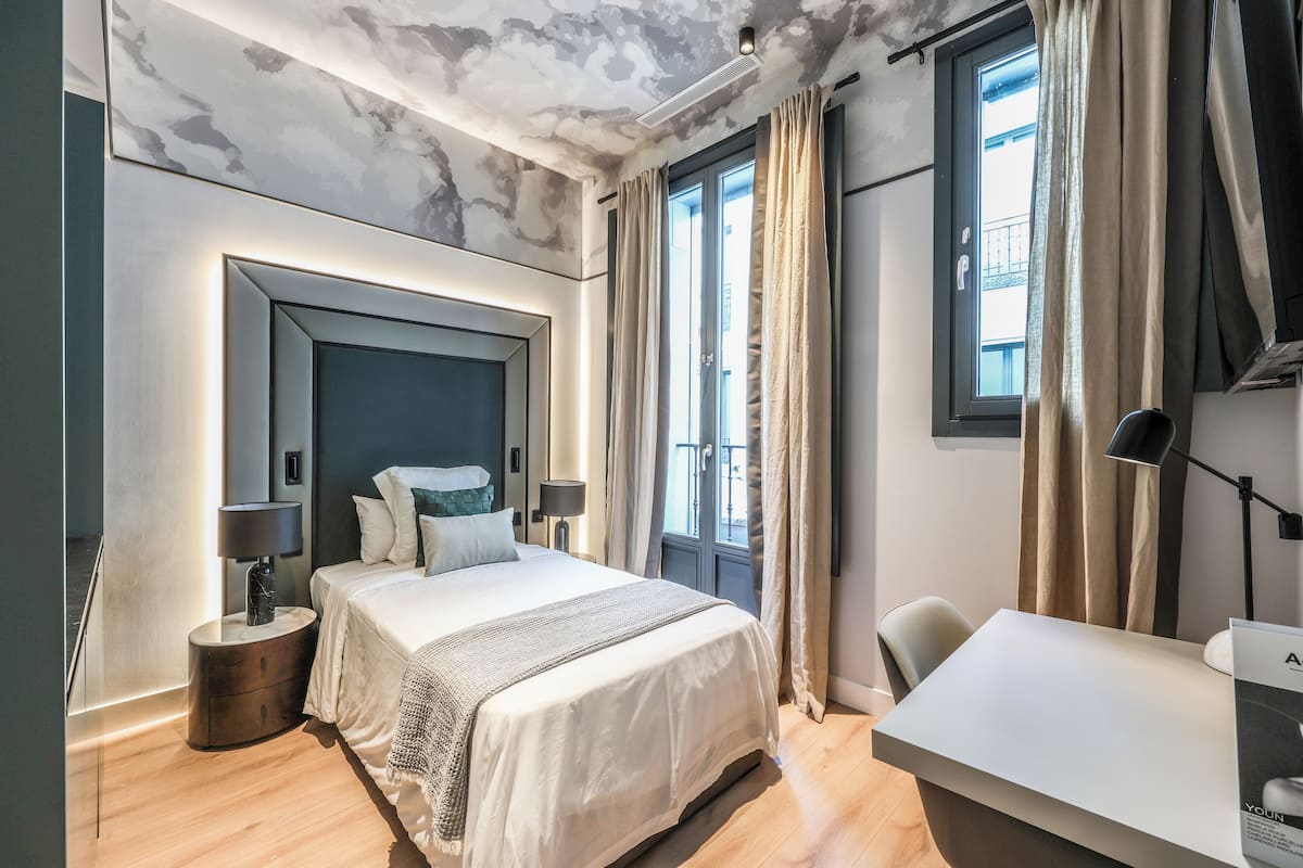 Een moderne slaapkamer met een groot bed, nachtlampjes, een bureau en uitzicht op de stad door het raam.