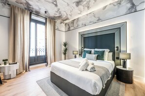 Une chambre d’hôtel moderne avec un grand lit, une table de chevet, une commode, un miroir et une vue sur l’extérieur.