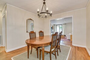 A dining room with a round wooden table, six chairs, a chandelier, and a large mirror on the wall. - Spacious Summerville Cottage (Augusta)