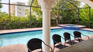 A swimming pool with a hot tub, surrounded by a pergola with chairs, and a view of buildings and trees in the background. - Closest Home to South Beach on Marco Island (Marco Island)