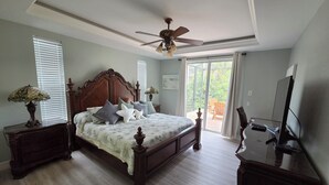 A bedroom with a bed, a ceiling fan, a TV, and a view through the window. - Closest Home to South Beach on Marco Island (Marco Island)
