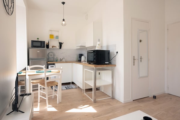 A compact kitchen with white cabinetry, a microwave, a coffee maker, and a small dining area with a table and chairs.