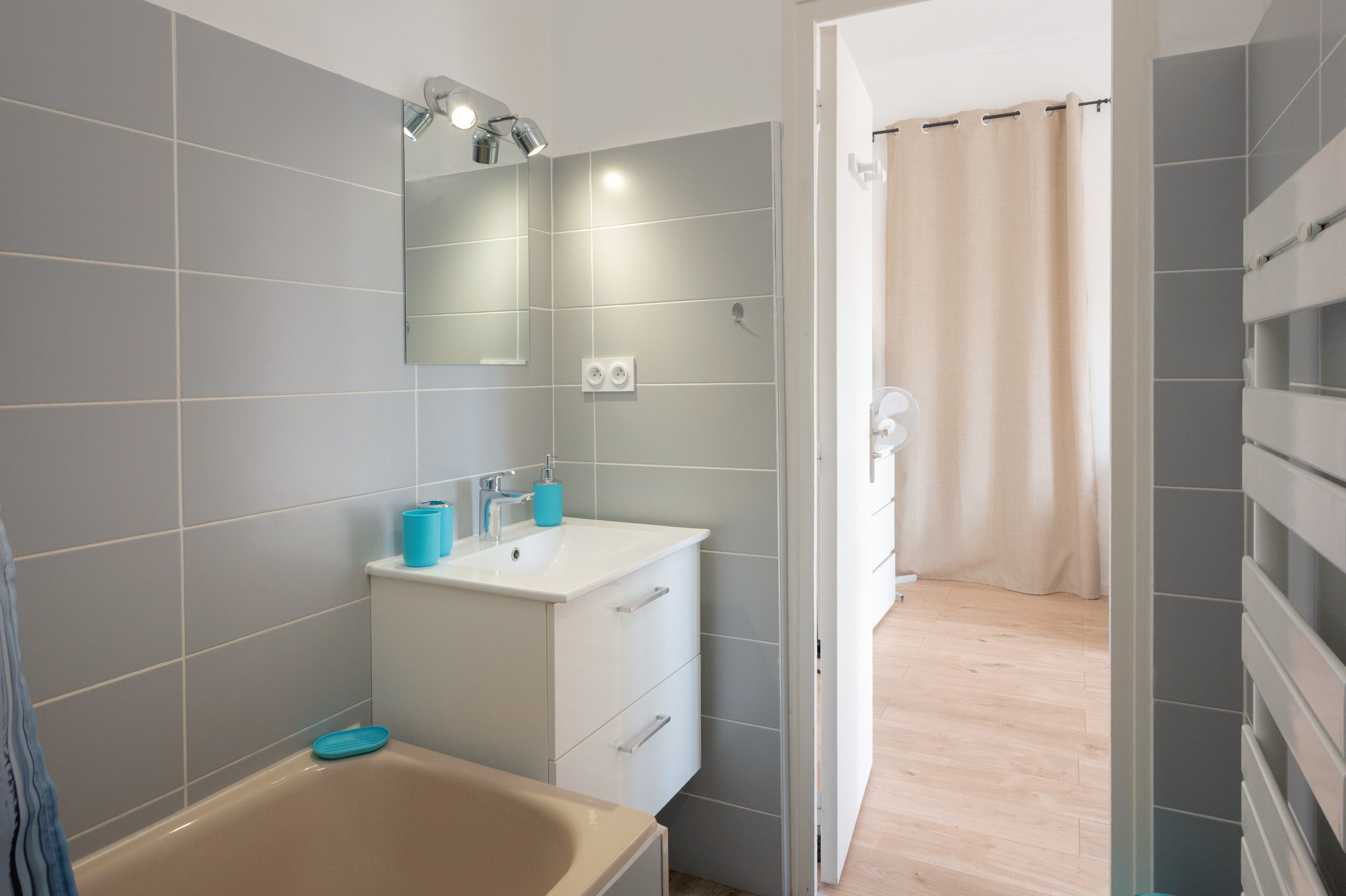 Un baño moderno con azulejos grises, un lavamanos blanco, un espejo y una bañera.