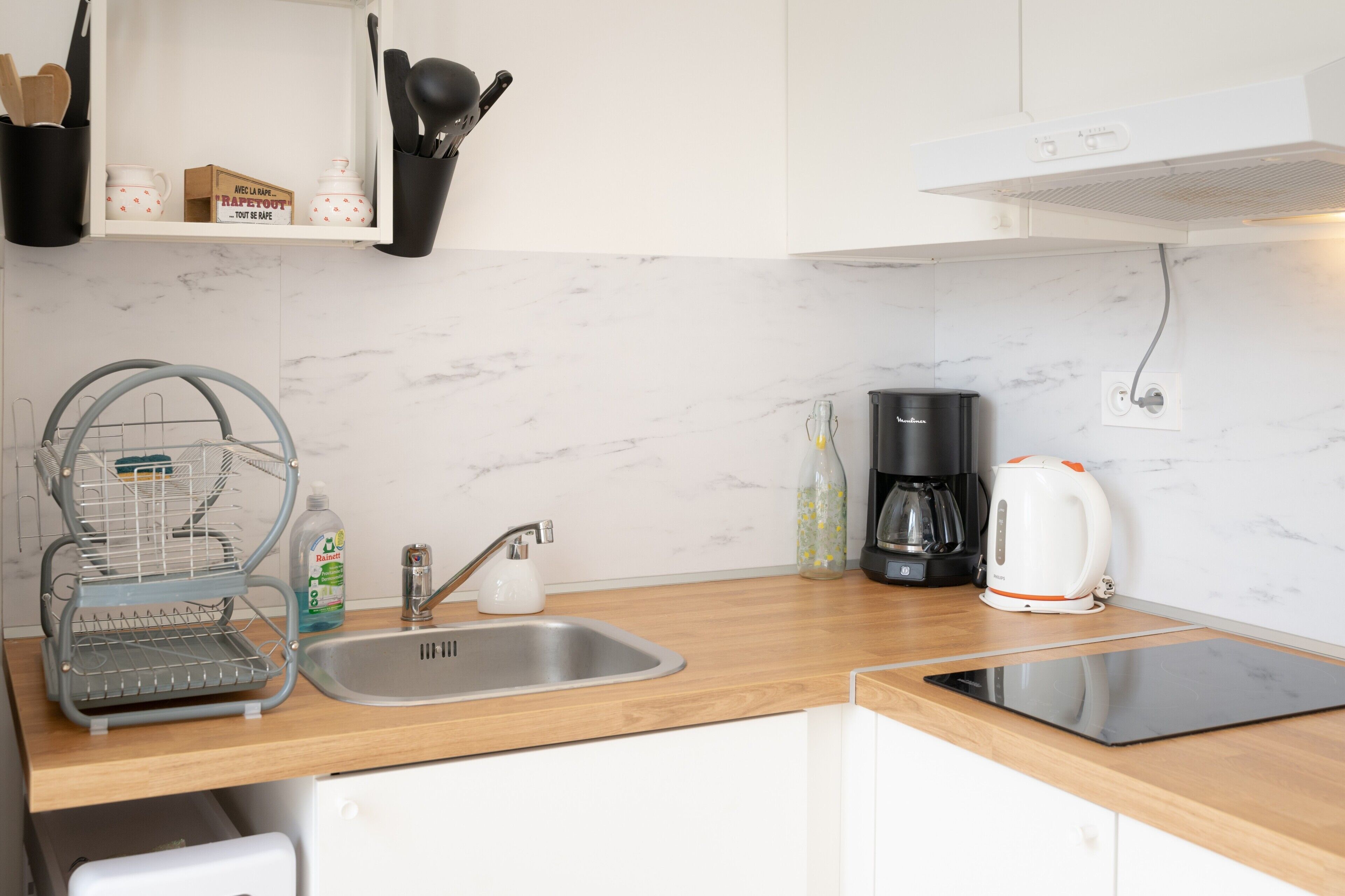 Una cocina con un lavamanos, escurreplatos, cafetera y una tableta en la encimera.