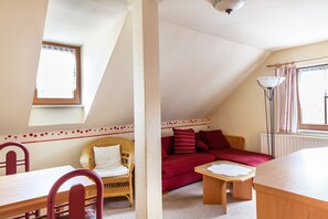 A cozy room with a dining table, wicker chair, red sofa, and a small wooden table.