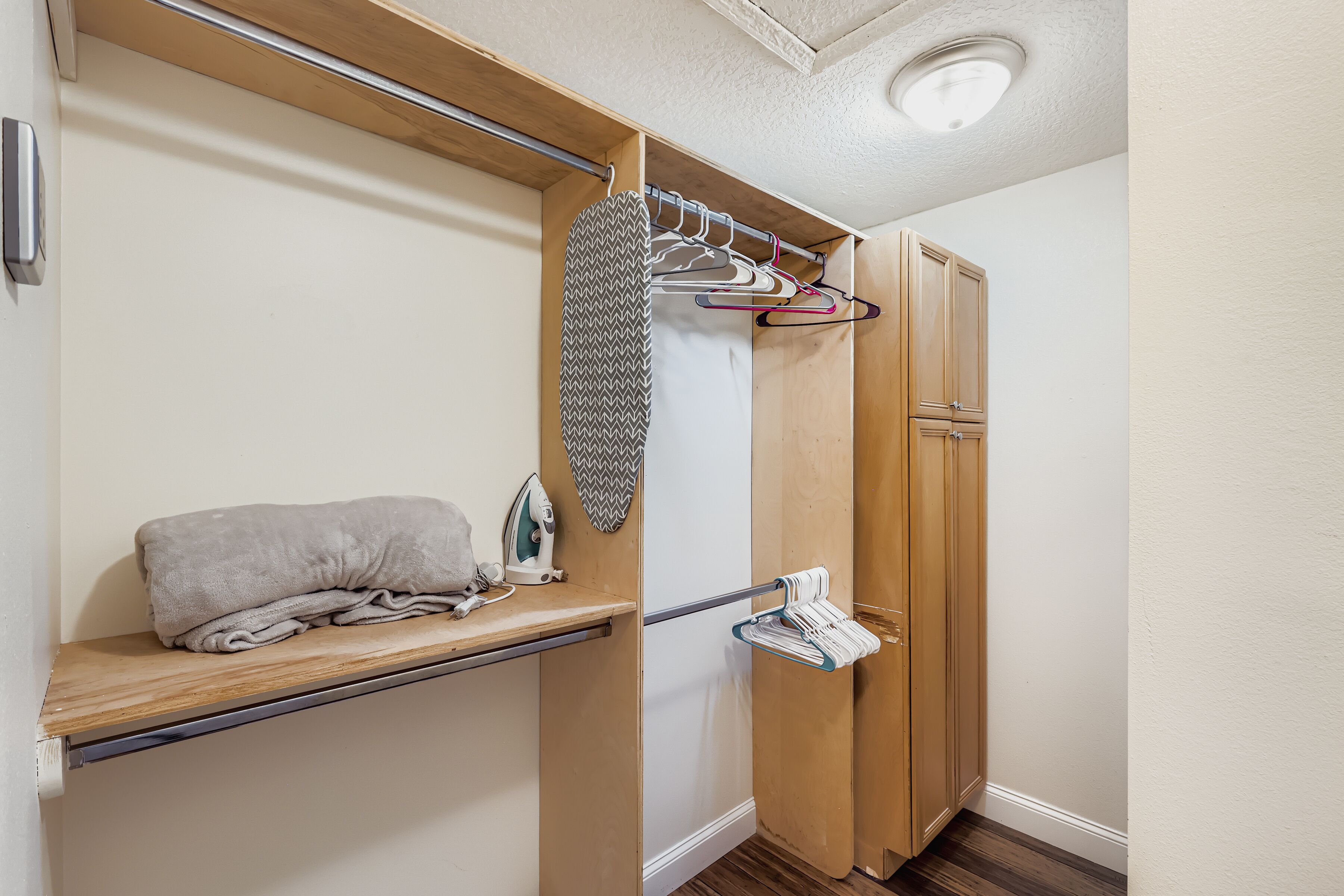 Una habitación compacta con plancha integrada, armario de madera y estante con toallas dobladas.