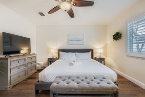 Ein Schlafzimmer mit einem großen Bett, einem Deckenventilator, einem Fernseher, Nachttischlampen und einem Fenster mit Jalousien.