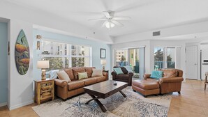 A spacious living room with a ceiling fan, two leather sofas, a coffee table, and a large window with blinds. - 🌅Gorgeous Unit | Perfect for Families | Great Amenities | Oceanwalk 7-301🌅 (New Smyrna Beach)