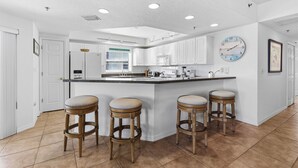 A modern kitchen with white cabinets, a large island with stools, and a clock on the wall. - 🌅Gorgeous Unit | Perfect for Families | Great Amenities | Oceanwalk 7-301🌅 (New Smyrna Beach)