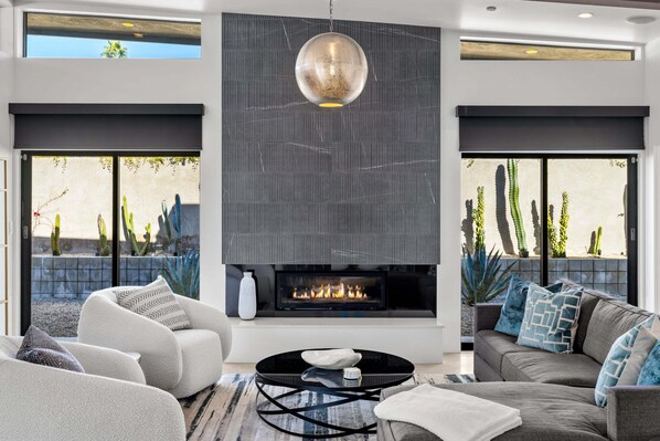 Una sala de estar moderna con chimenea, asientos cómodos y grandes ventanales con vistas a un paisaje desértico.