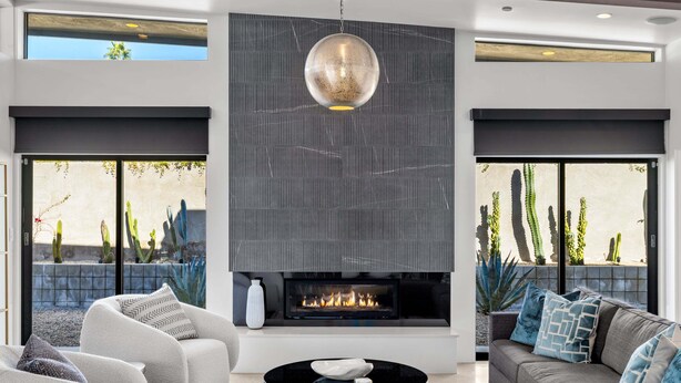 A modern living room with a fireplace, comfortable seating, and large windows overlooking a desert landscape. - Audrey's on Park - Luxury Sunrise Pool Estate (Palm Springs)