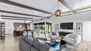 A modern living room with a sofa, a coffee table, and a TV. - Audrey's on Park - Luxury Sunrise Pool Estate (Palm Springs)