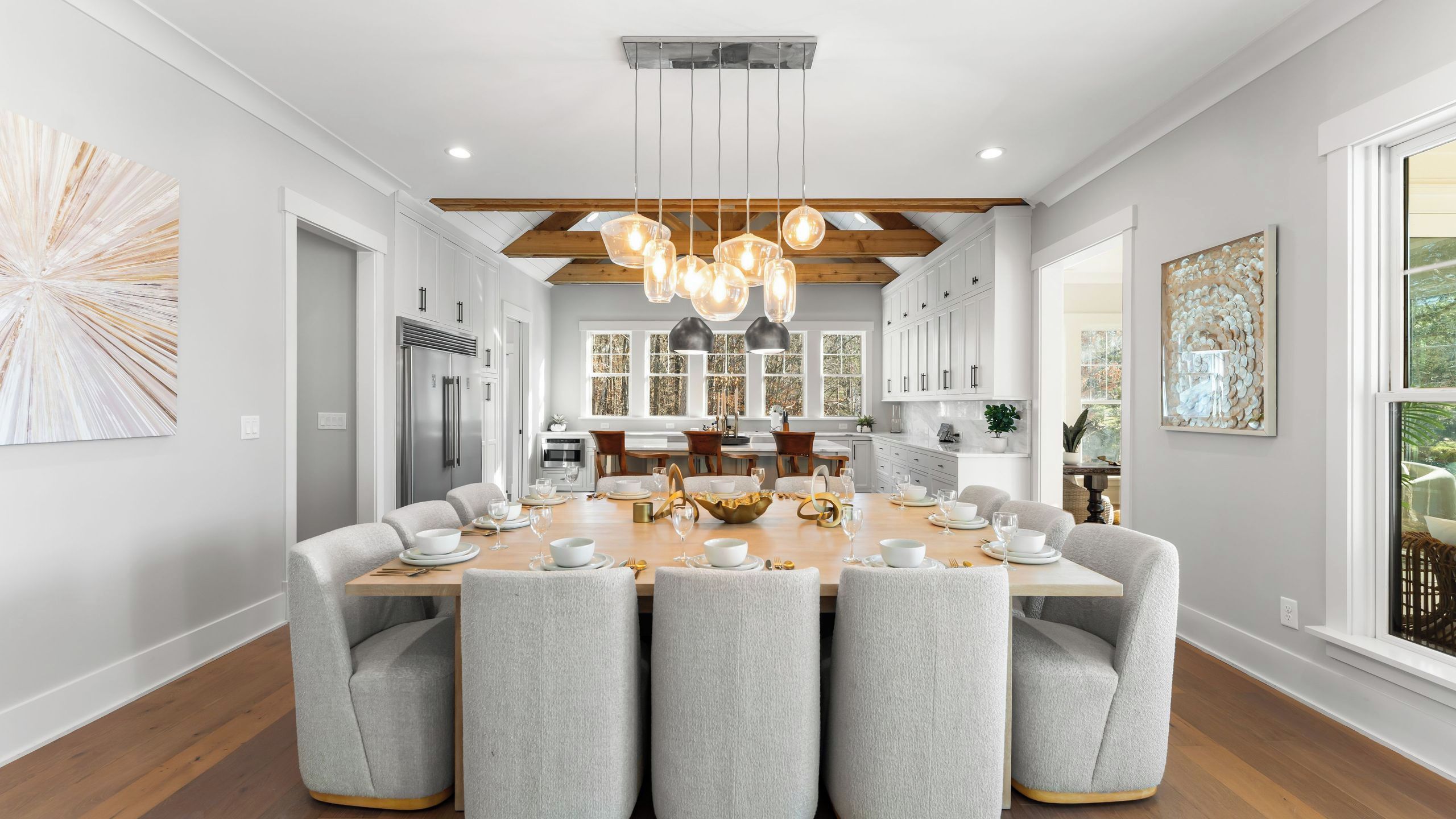 A modern dining room with a large table, chairs, and pendant lighting.