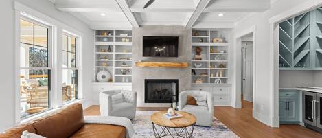 A modern living room with a fireplace, white shelving, and a dining area.
