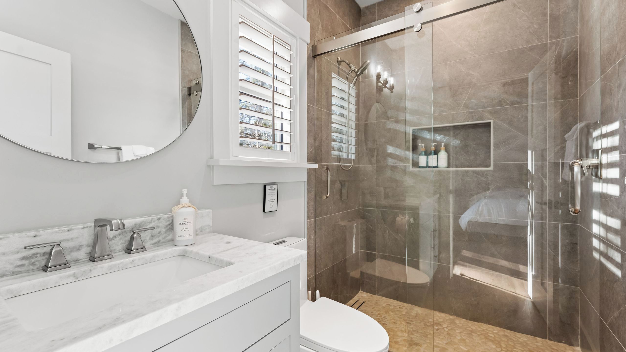 A modern bathroom with a marble sink, a toilet, and a glass-enclosed shower.