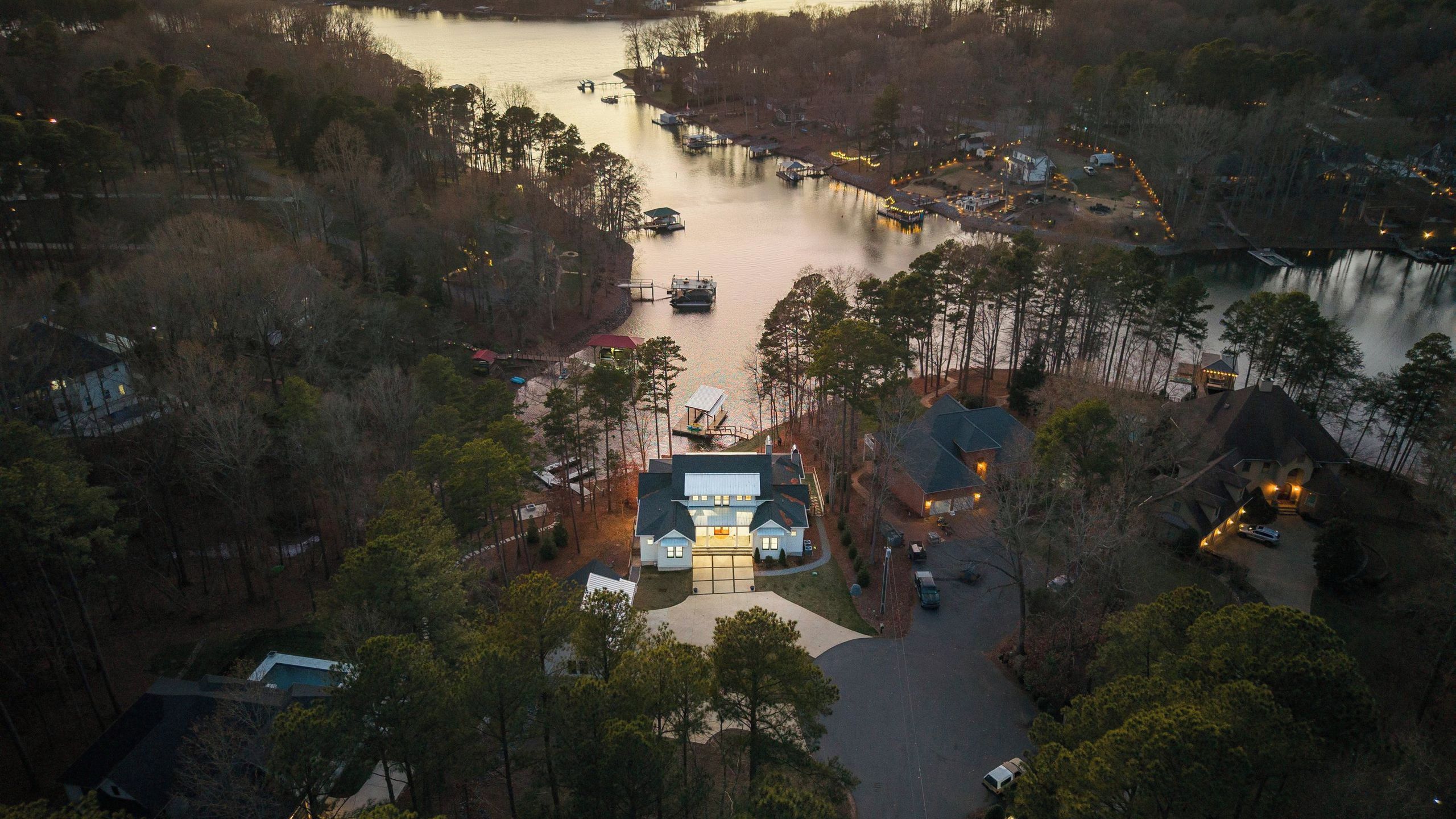 An aerial view of a lakeside property with a large house, docked boats, and surrounding trees.