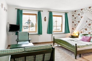 Een kamer met een bed, een bureau met stoel, een televisie en een raam met gordijnen.