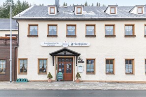 Ein Gebäude mit einem Schild, auf dem 'Landgasthof & Pension' und 'Frischhütte' steht, mit einer traditionellen Fassade, mehreren Fenstern und einem zentralen Eingang.