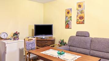 Uma sala de estar com televisão, sofá, mesa de jantar e um relógio em uma mesinha.