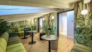 Un espace de détente moderne avec des sièges recouverts d’un tissu vert, des tables rondes et un plafond doté de poutres apparentes et d’une verrière.