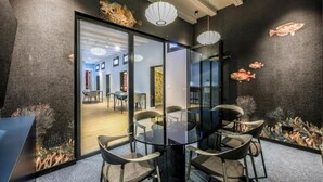 Une salle de réunion moderne, dotée d’une table et de chaises en verre, d’un mur texturé de couleur sombre et d’une fresque représentant des poissons.