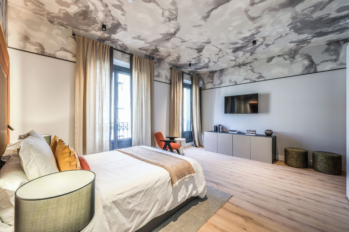 Et moderne hotelværelse med en stor seng, et fladskærms-tv, et skrivebord og et siddeområde med stol og bord.