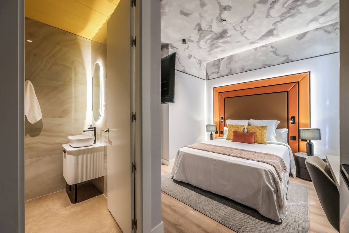A modern hotel room with a marble bathroom, a large bed with multiple pillows, and a wooden headboard.