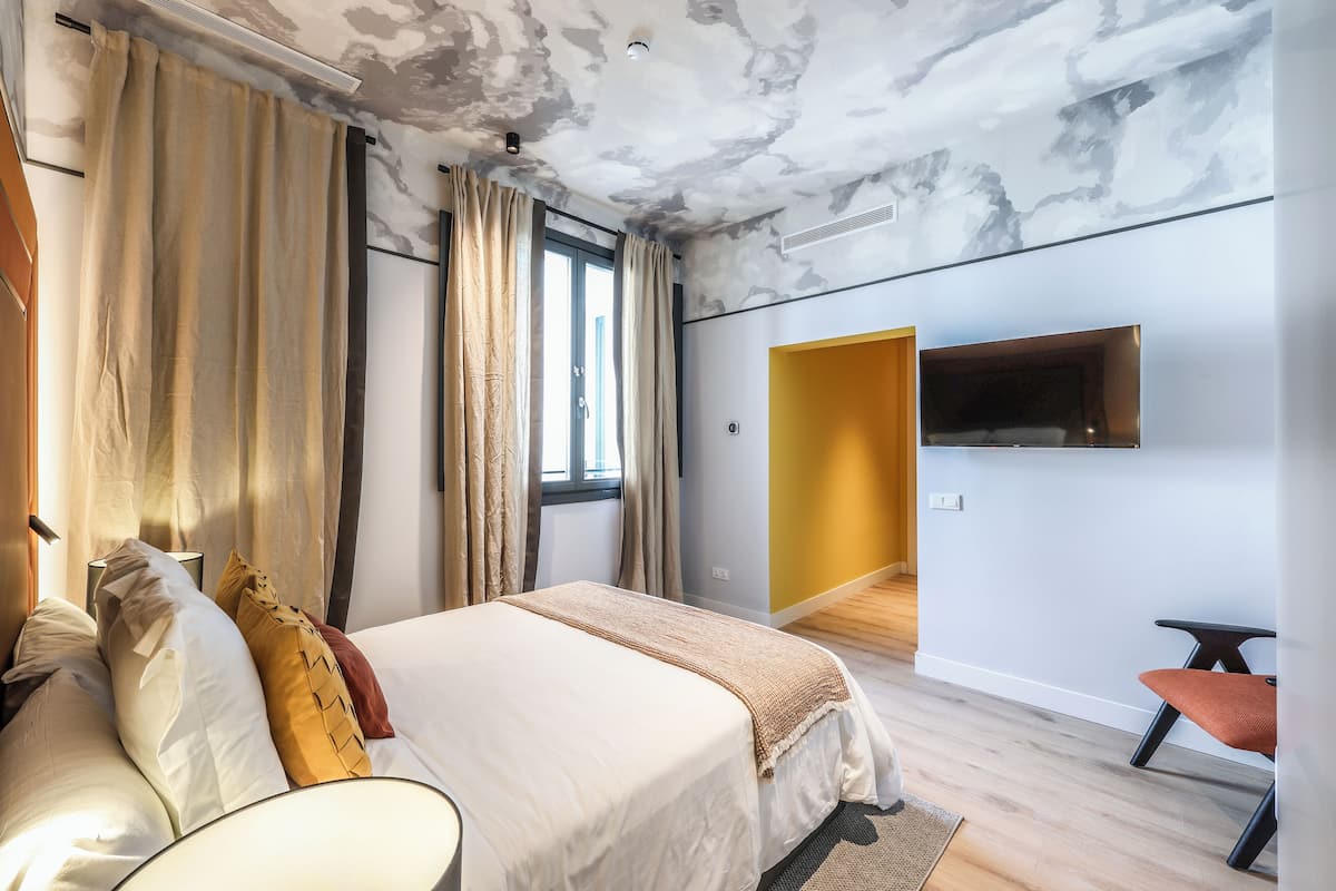 A modern bedroom with a bed, curtains, a TV, and a small seating area.