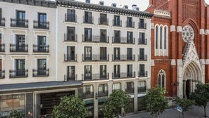 Une rangée d’immeubles à étages dotés de balcons, une église à l’architecture complexe et une rue bordée d’arbres et dotée d’un trottoir.