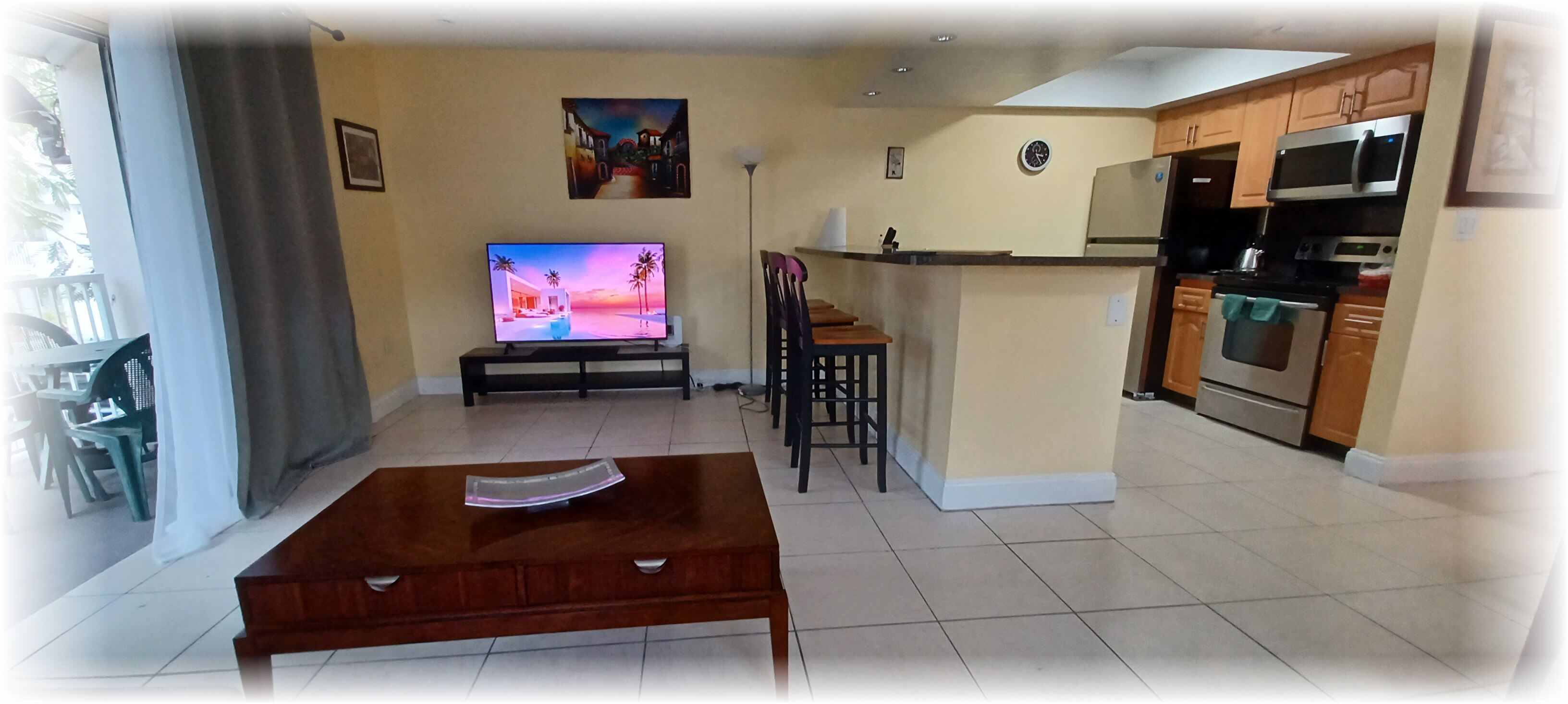 A living room with a TV, a wooden coffee table, a kitchen with modern appliances, and a dining area with chairs.