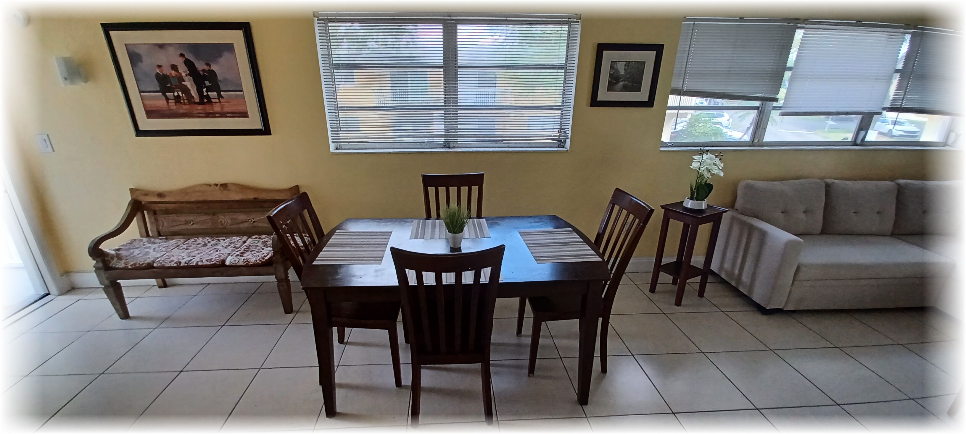 A dining area with a wooden table and chairs, a sofa, and a window with blinds.