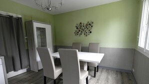 A dining area with a white table and chairs, a cabinet, and a decorative wall piece. - Le Corot - T2 near city center (Saint-Brieuc)