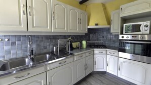 A kitchen with white cabinets, a stainless steel sink, a microwave, and a stove. - Le Corot - T2 near city center (Saint-Brieuc)