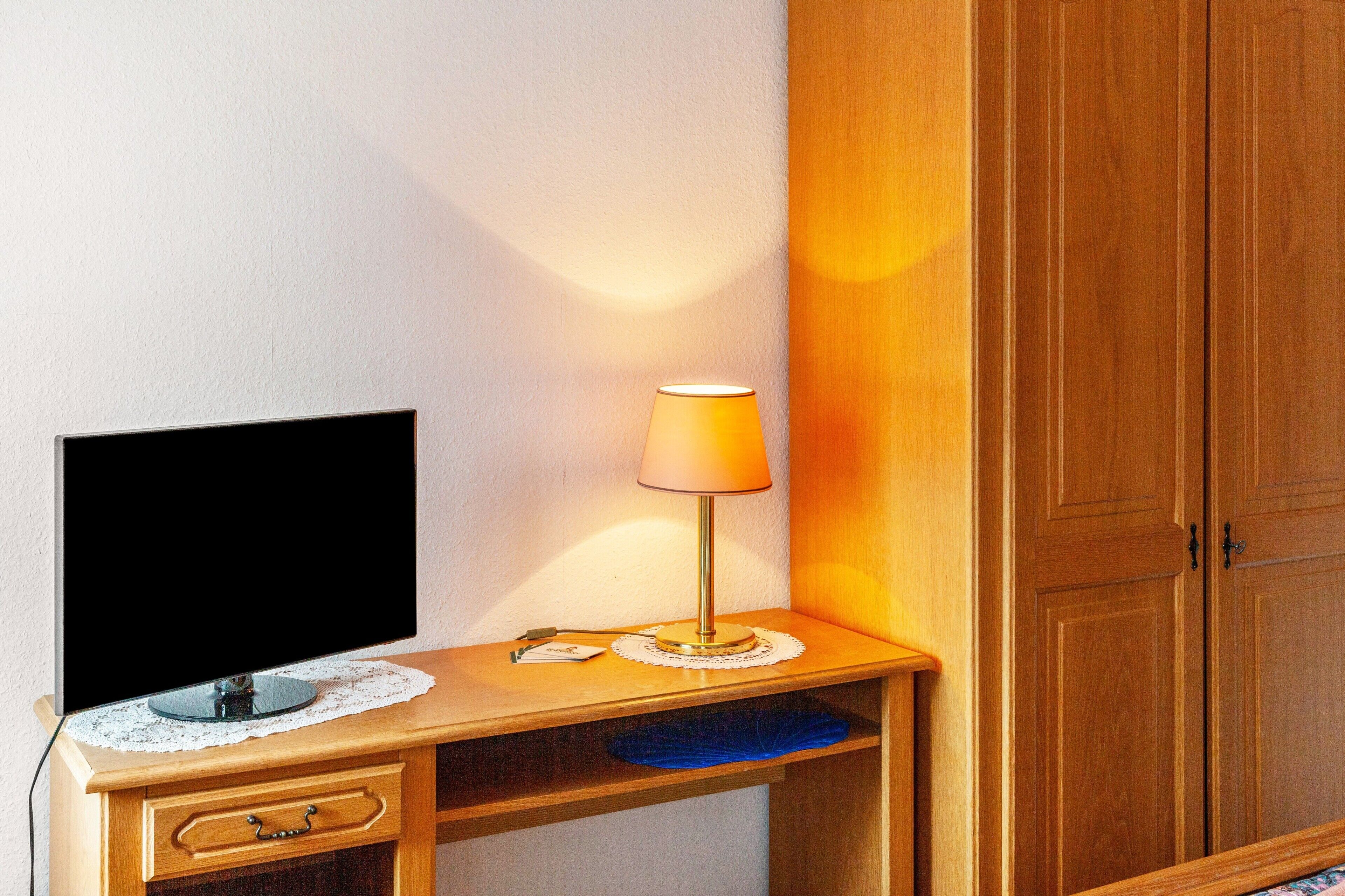 Et træskrivebord med et fjernsyn, en lampe og en lille blå genstand på hylden.