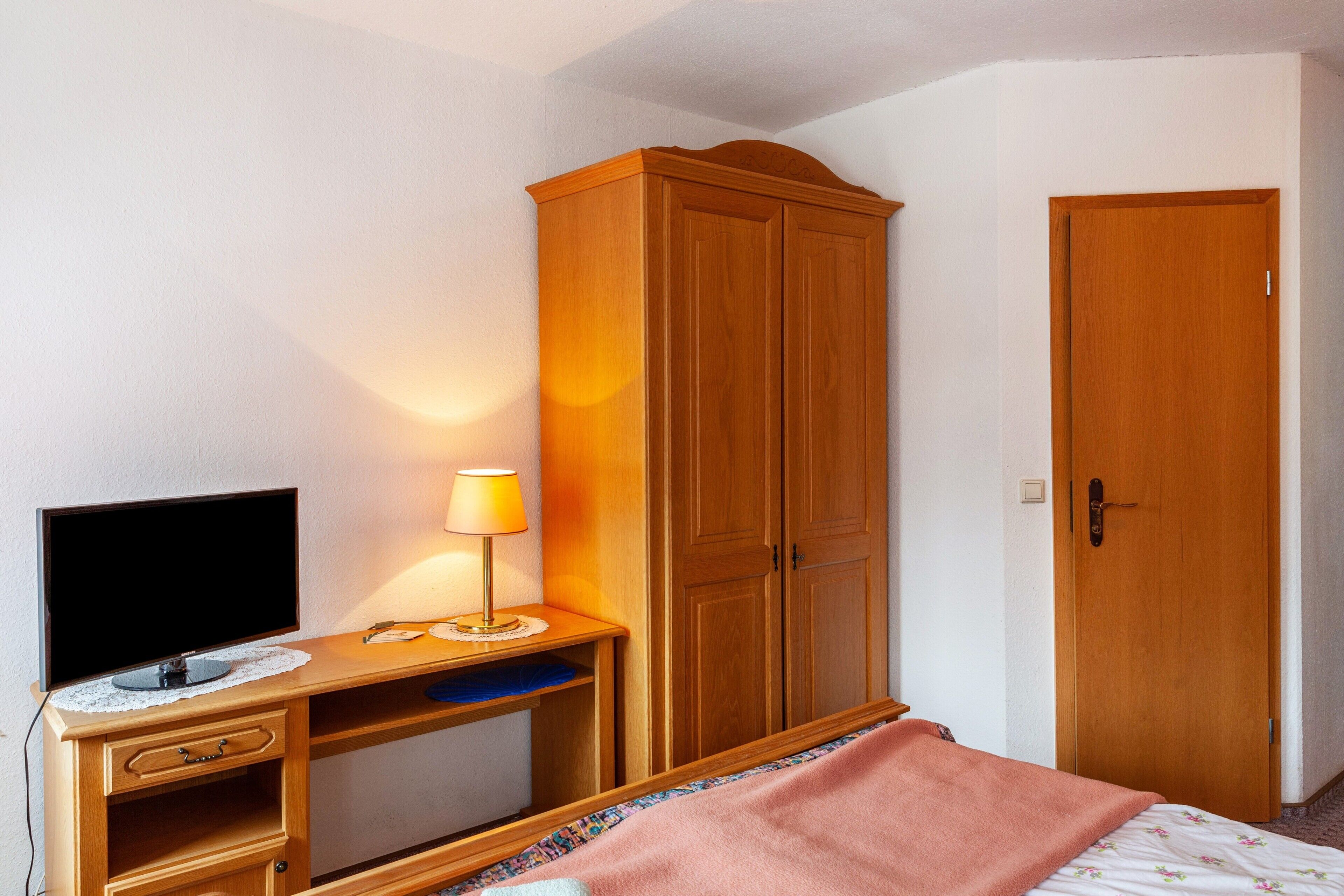 Un dormitorio con cama, escritorio con televisor, armario y puerta.