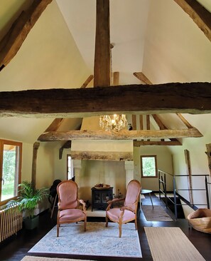 Un intérieur rustique avec des poutres apparentes, une cheminée, deux fauteuils à rayures et une table à manger.