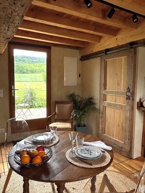 Een houten eettafel met uitzicht op een groen landschap door een geopende deur.