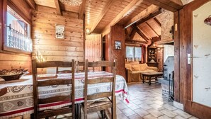 Een houten interieur met een eettafel, stoelen, een open haard en een keukenhoek.