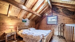 Een slaapkamer in een houten chalet, met een bed, nachtkastje en een raam met decoratief glas.