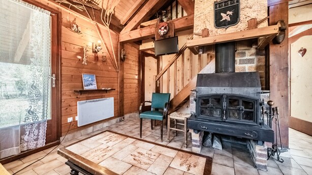 Een houten interieur met een open haard, een trap en een raam met kantgordijnen.
