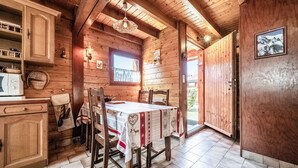 Een houten interieur met een eettafel, stoelen, een raam en een deur die naar buiten leidt.