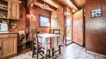 A wooden interior with a dining table, chairs, a window, and a door leading outside.
