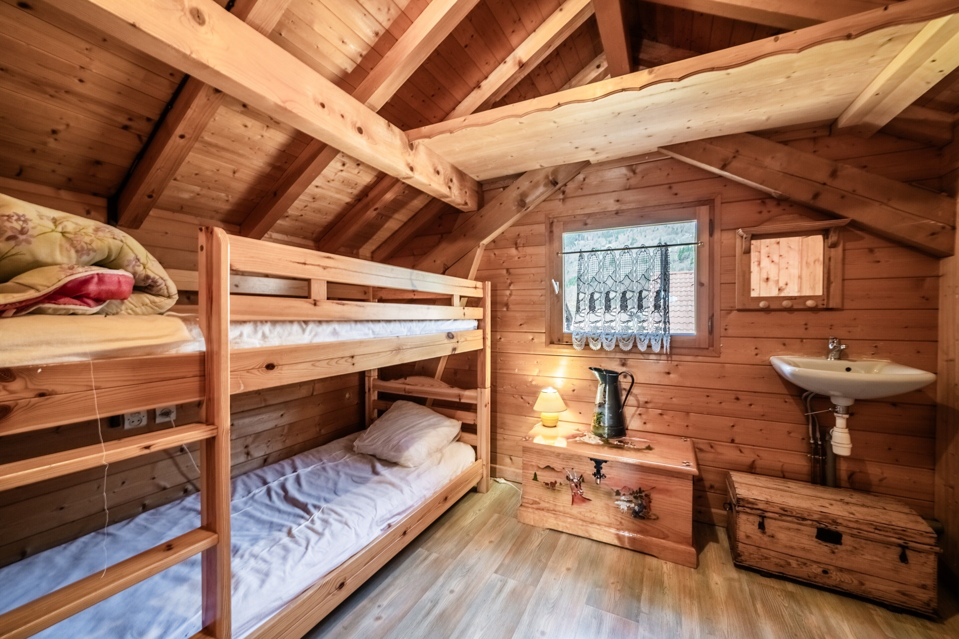 A wooden cabin with bunk beds, a window with a view, a sink, and a small cabinet.
