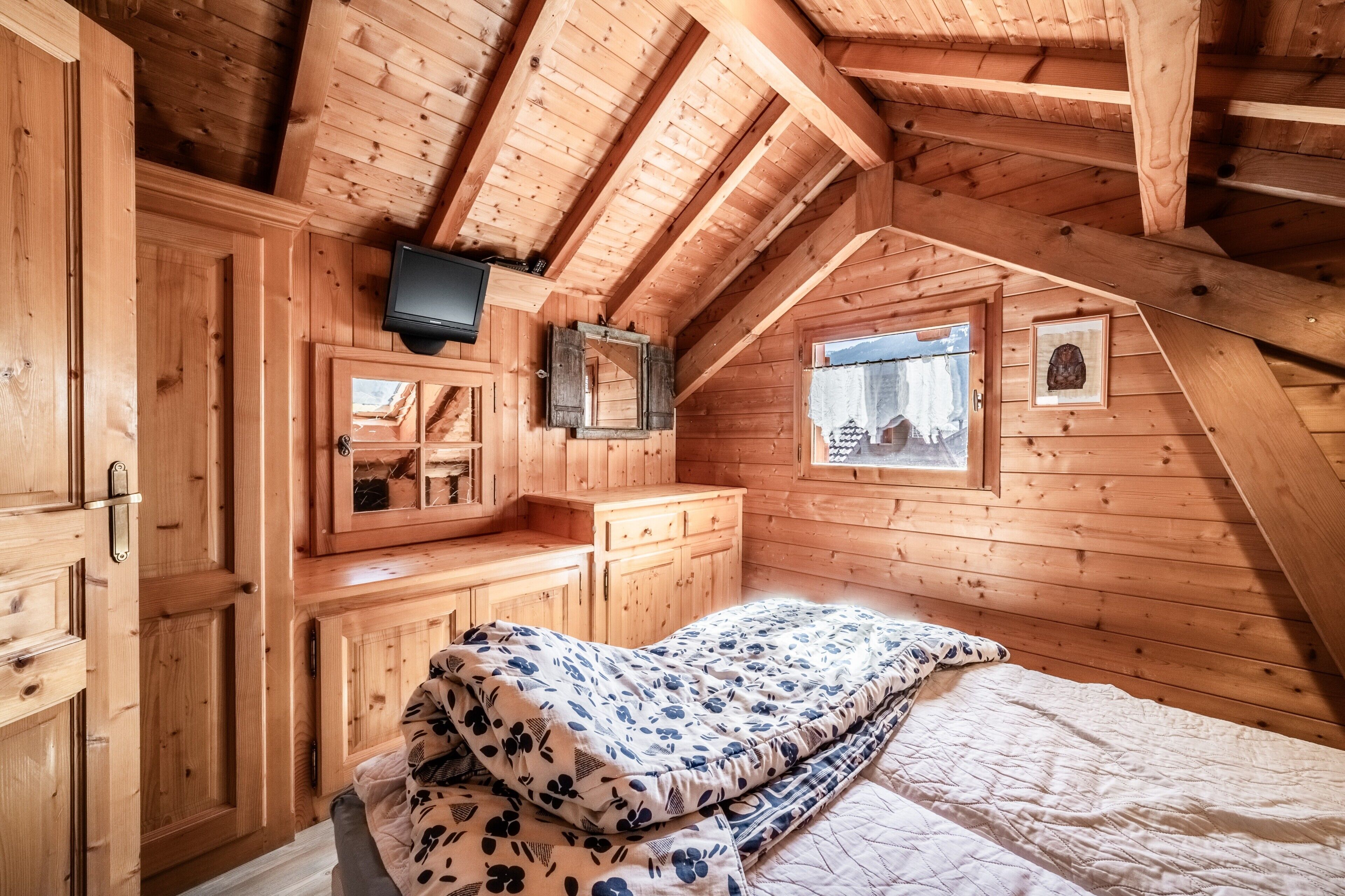 Camera da letto in una baita di legno con un letto, una televisione, una finestra e uno specchio.