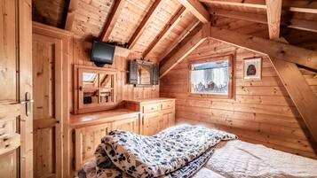 Camera da letto in una baita di legno con un letto, una televisione, una finestra e uno specchio.